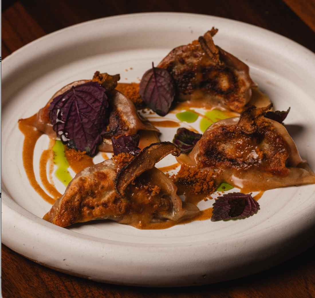Seared gyoza with chili sauce and shiso on a cream stoneware plate