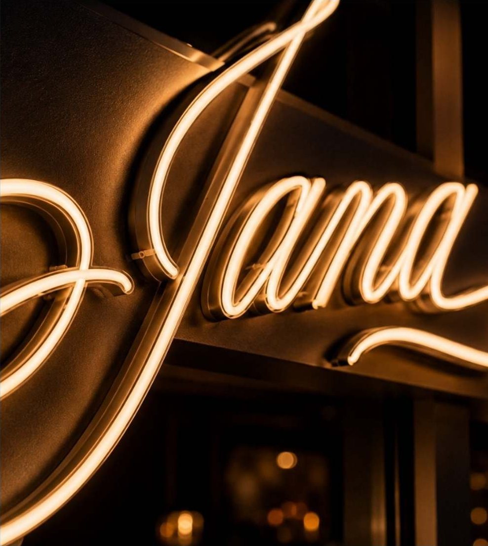 The Jana neon script sign in warm white above the entrance